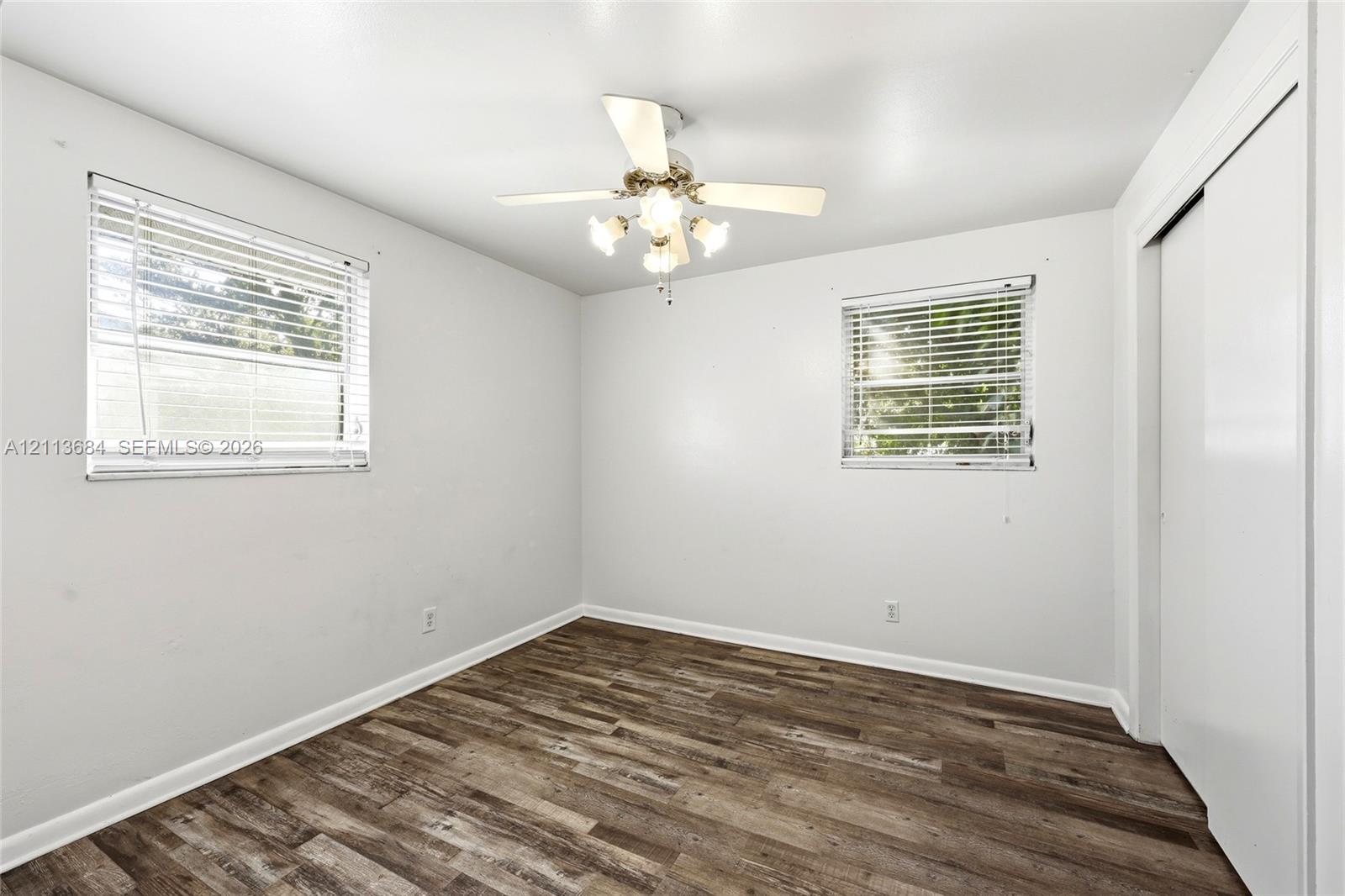 Wood-finish flooring, dual windows with horizontal blinds, ceiling fan with integrated light fixture, and white closet doors