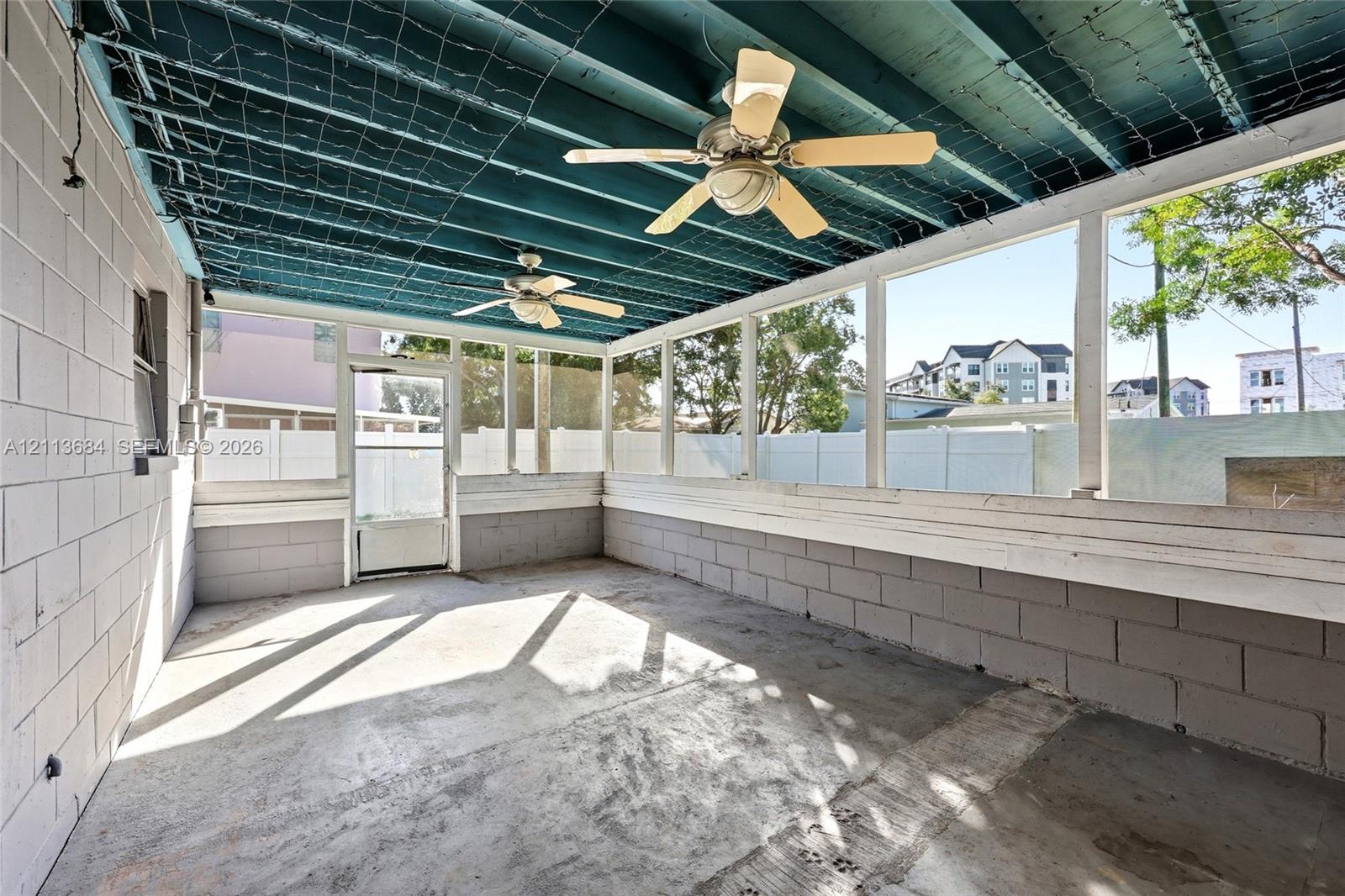 Screened-in porch featuring painted concrete block walls, a concrete floor, two ceiling fans, and an exposed ceiling structure