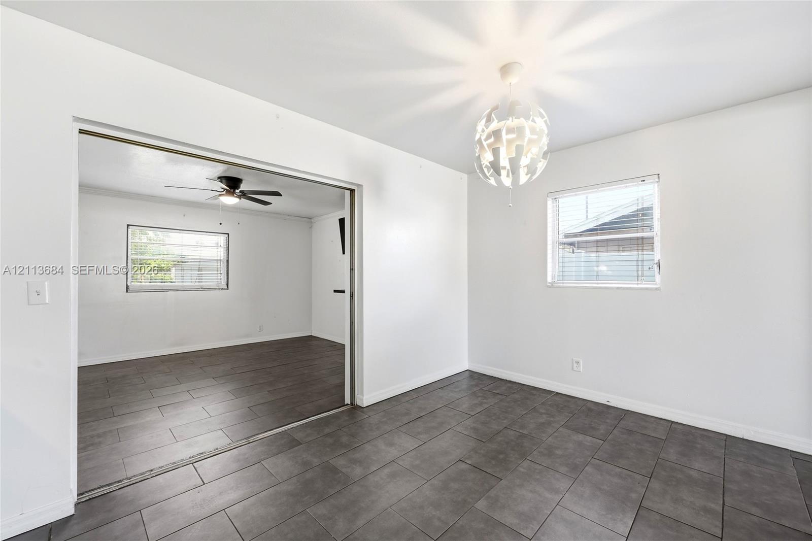 Large-format ceramic tile flooring, decorative multi-tiered pendant lighting, and neutral wall finishes, complemented by horizontal sliding windows and a ceiling fan with integrated lighting