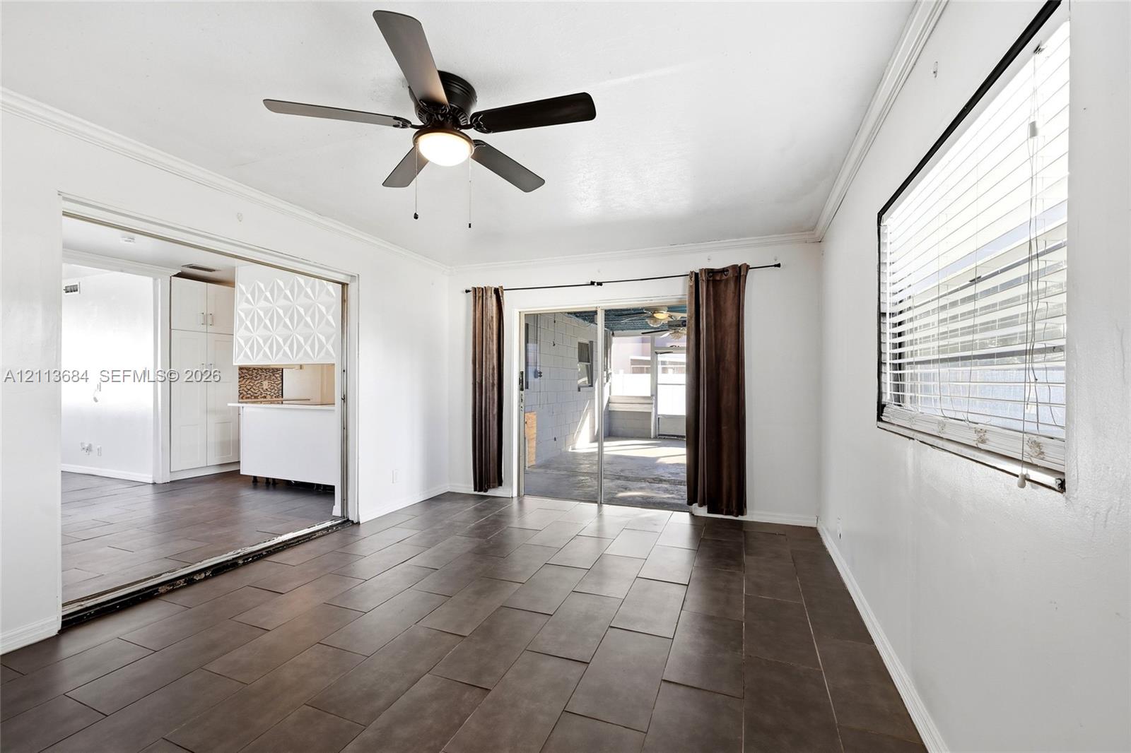 Neutral-toned tile flooring, ceiling fan with integrated lighting, oversized horizontal sliding glass door, and crown molding
