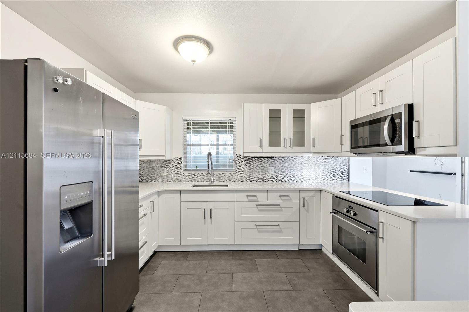 Kitchen featuring white cabinetry, stainless steel appliances, patterned tile backsplash, light-colored countertops, and tile flooring