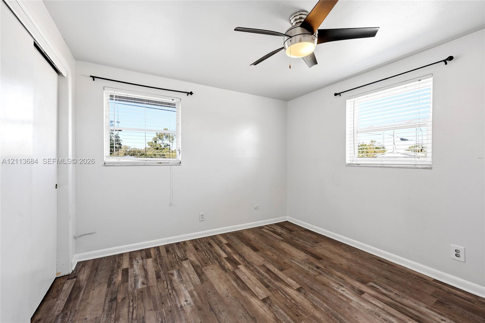 Wood-finish flooring, dual windows with mounted hardware, and a ceiling fan with integrated lighting