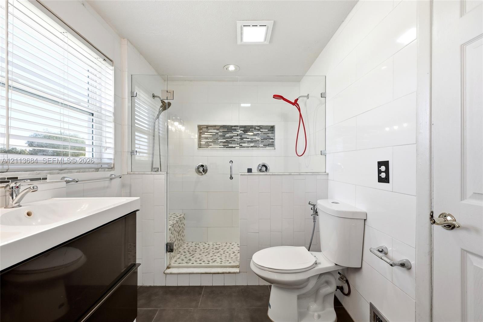 Walk-in shower with frameless glass enclosure, pebble-stone flooring, horizontal mosaic tile inlay, and wall-mounted plumbing fixtures, paired with a modern dark-finish vanity