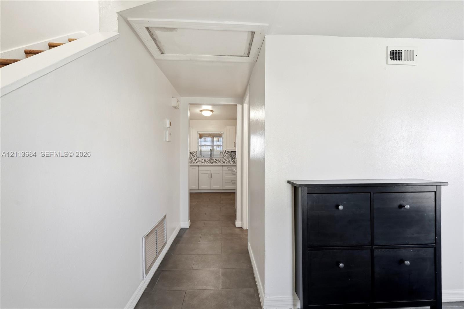 Interior hallway featuring large-format grey tile flooring, neutral wall finishes, and recessed ceiling access Interior hallway featuring large-format grey tile flooring, neutral wall finishes, and recessed ceiling access