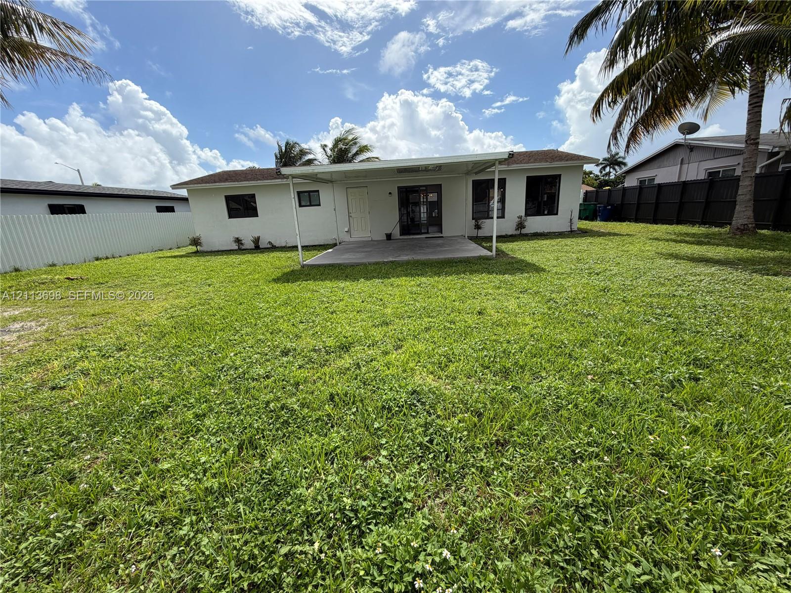 Expansive backyard featuring a covered concrete patio, solid perimeter fencing, and mature palm trees