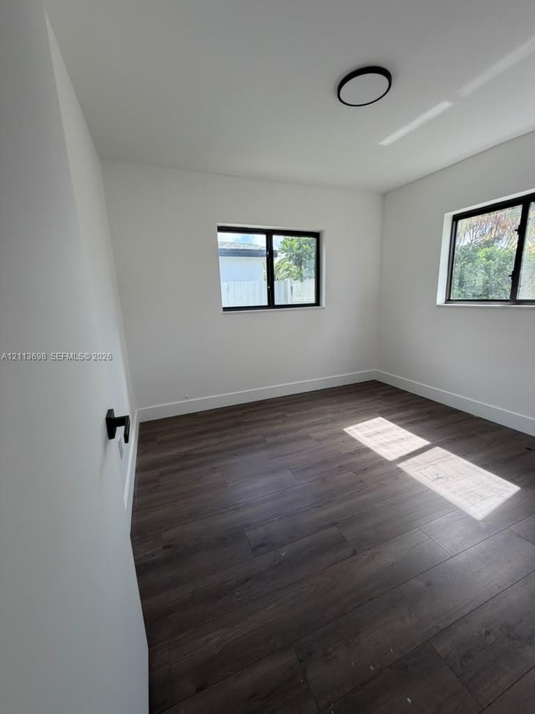 Interior room featuring wood-finish flooring, two windows with black frames, and a flush-mount ceiling light