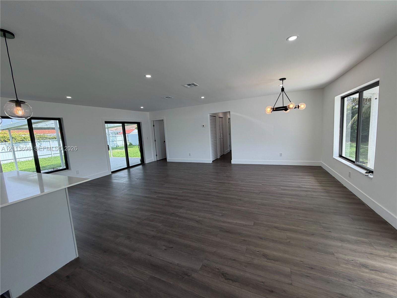 Open-concept interior featuring wood-finish flooring, recessed lighting, multi-arm chandelier, and sliding glass doors with dark frames