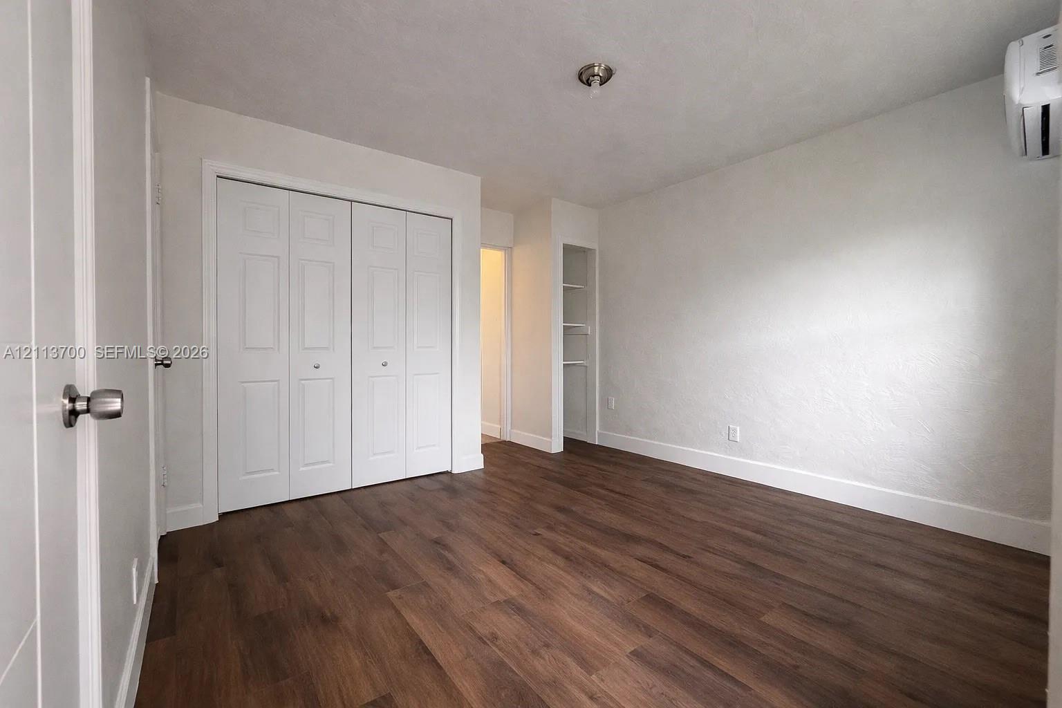 Interior room featuring wood-finish flooring, a wall-mounted ductless mini-split unit, white bi-fold closet doors, and recessed built-in shelving