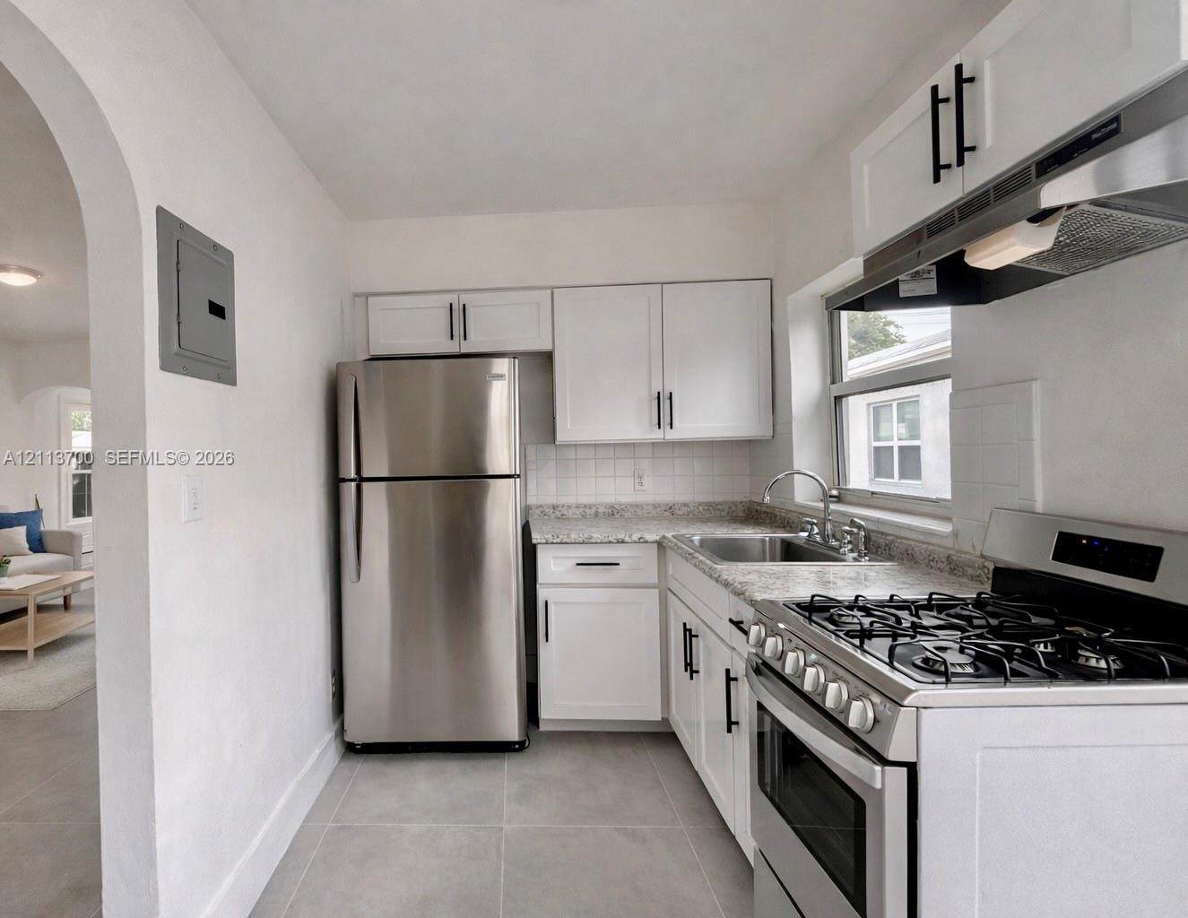 Kitchen featuring white shaker-style cabinetry with matte black hardware, stone-patterned countertops, stainless steel appliances, and large-format tile flooring Kitchen featuring white shaker-style cabinetry with matte black hardware, stone-patterned countertops, stainless steel appliances, and large-format tile flooring