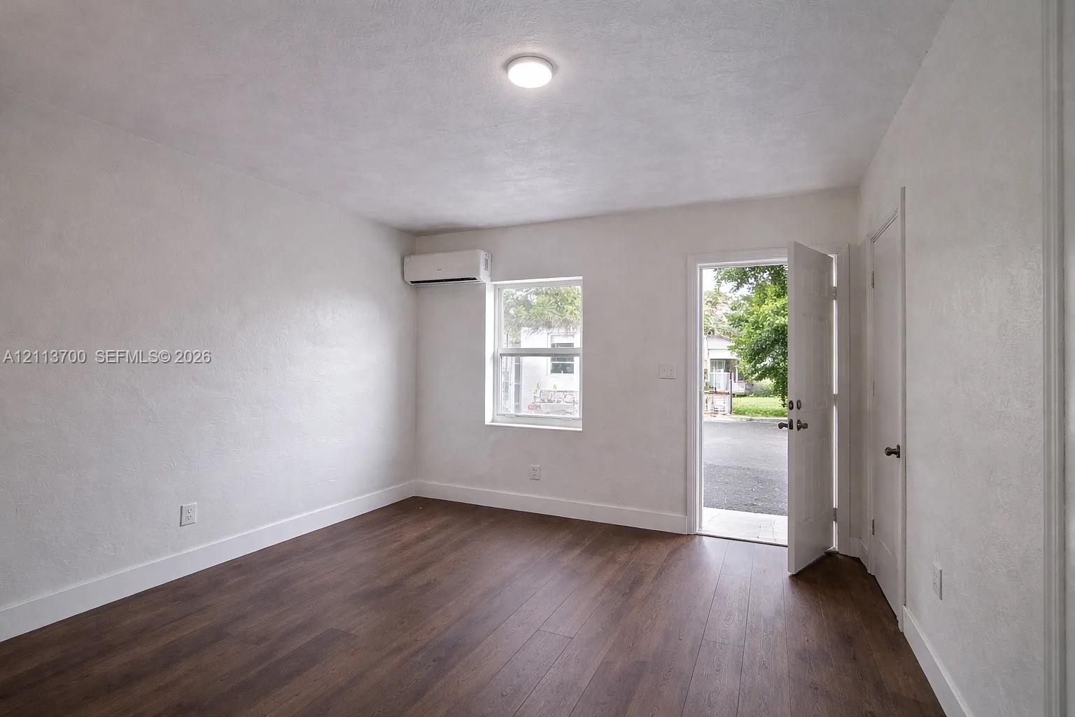 Room featuring wood-finish flooring, a wall-mounted ductless mini-split climate control unit, a single-hung window, and a flush-mount ceiling light fixture