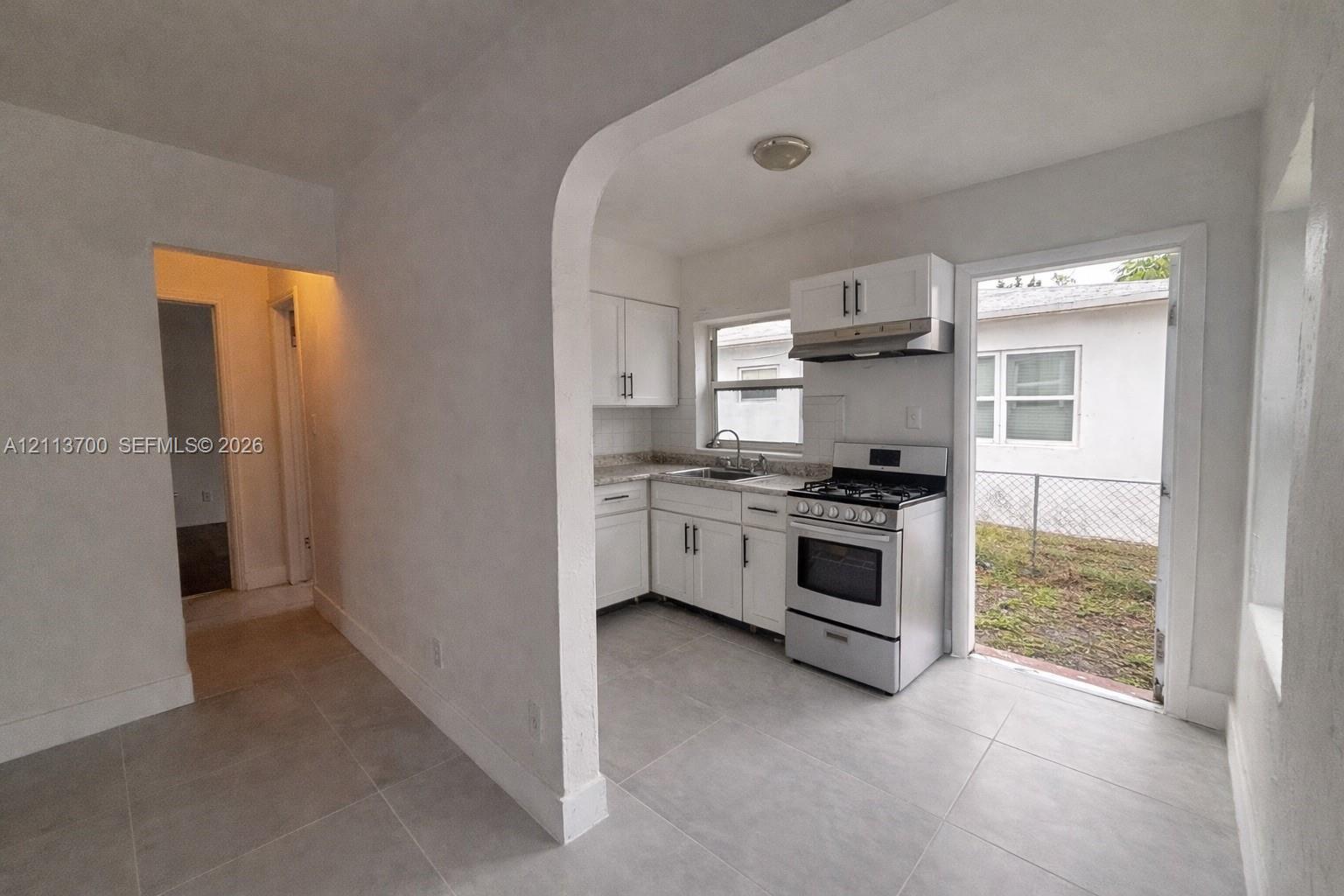 Kitchen featuring white cabinetry, stone-finish countertops, tile flooring, and a stainless steel gas range with an integrated vent hood Kitchen featuring white cabinetry, stone-finish countertops, tile flooring, and a stainless steel gas range with an integrated vent hood