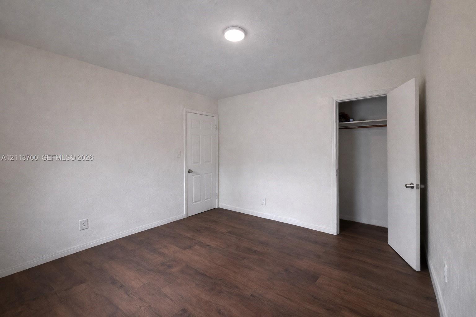 Neutral-toned interior space featuring wood-finish flooring, a recessed closet with built-in shelving, a panel door, and a flush-mount ceiling light fixture