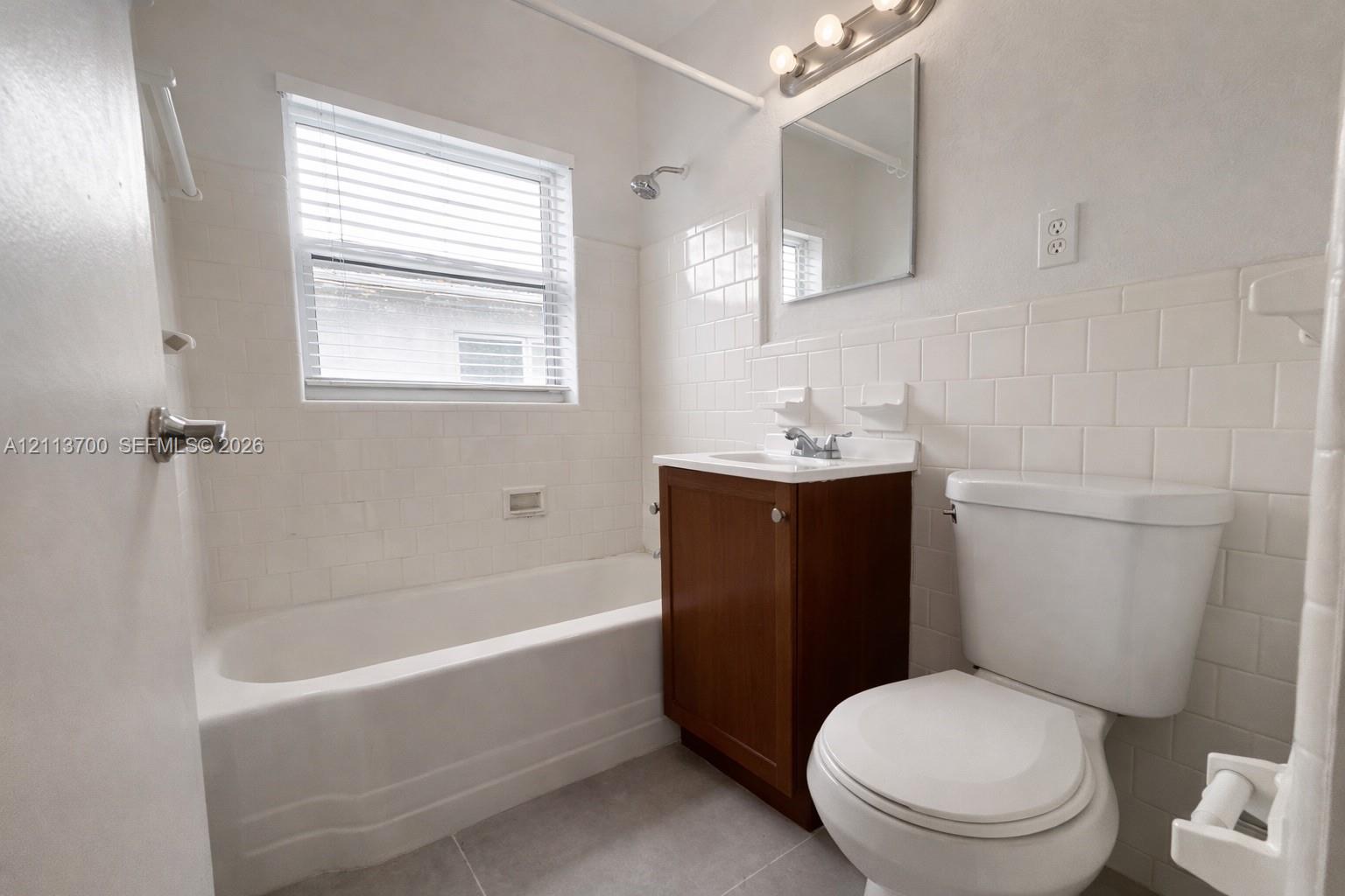 Bathroom featuring a single-sink vanity with a wood-finish cabinet, white subway tile shower surround, standard bathtub, and wall-mounted vanity lighting