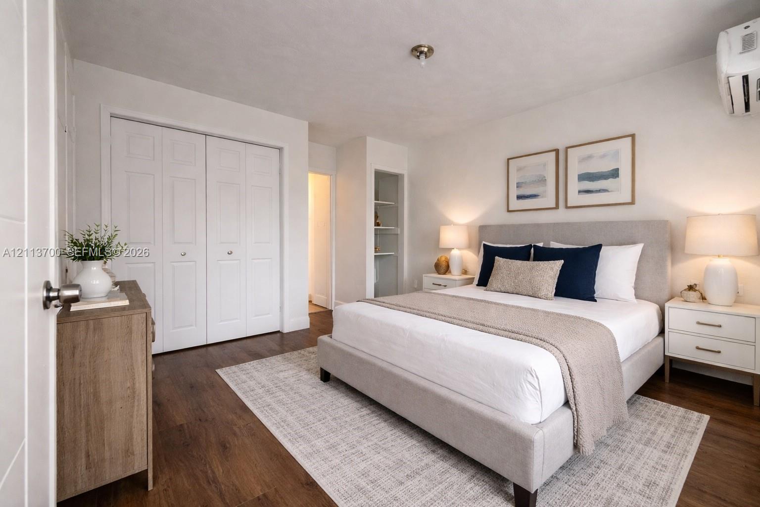 Wood-finish flooring, double-door closet with recessed paneling, built-in open shelving, and wall-mounted climate control unit Wood-finish flooring, double-door closet with recessed paneling, built-in open shelving, and wall-mounted climate control unit