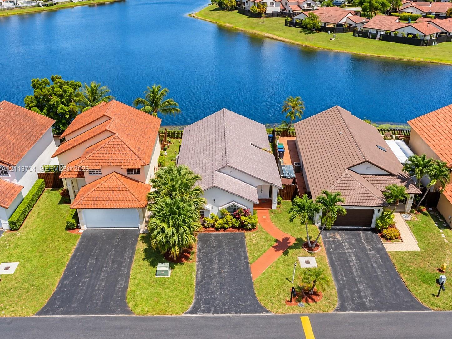 Waterfront residential properties featuring tile roofing, paved driveways, and mature landscaping Waterfront residential properties featuring tile roofing, paved driveways, and mature landscaping