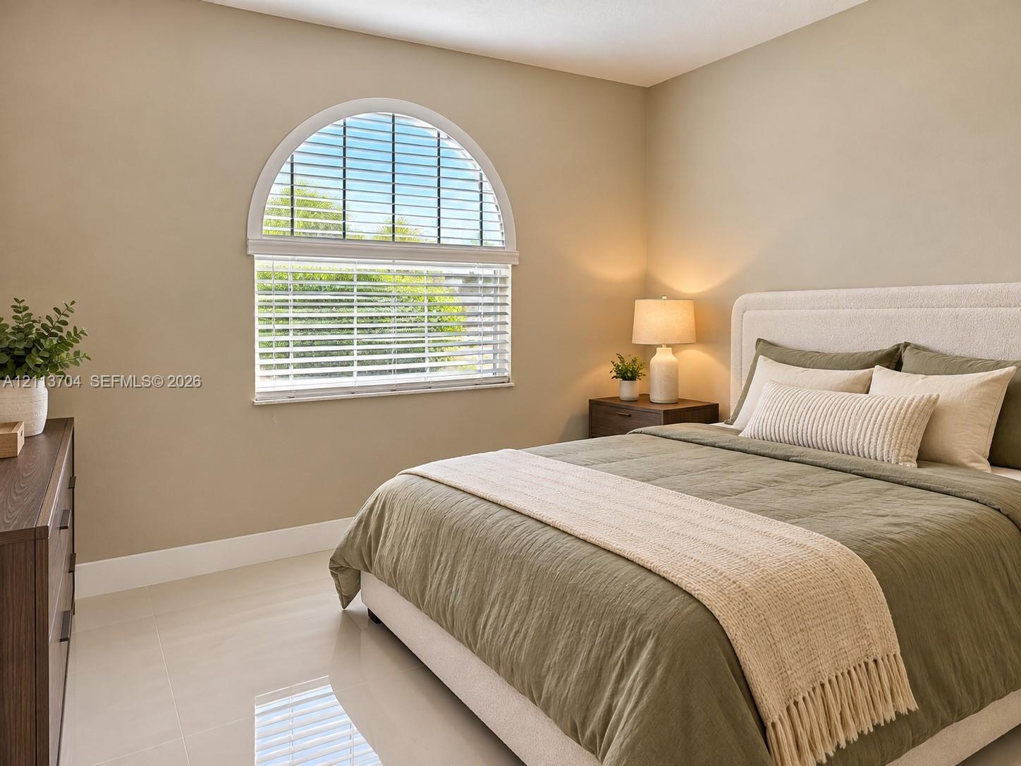 Room featuring neutral wall paint, polished tile flooring, and an arched window with horizontal blinds