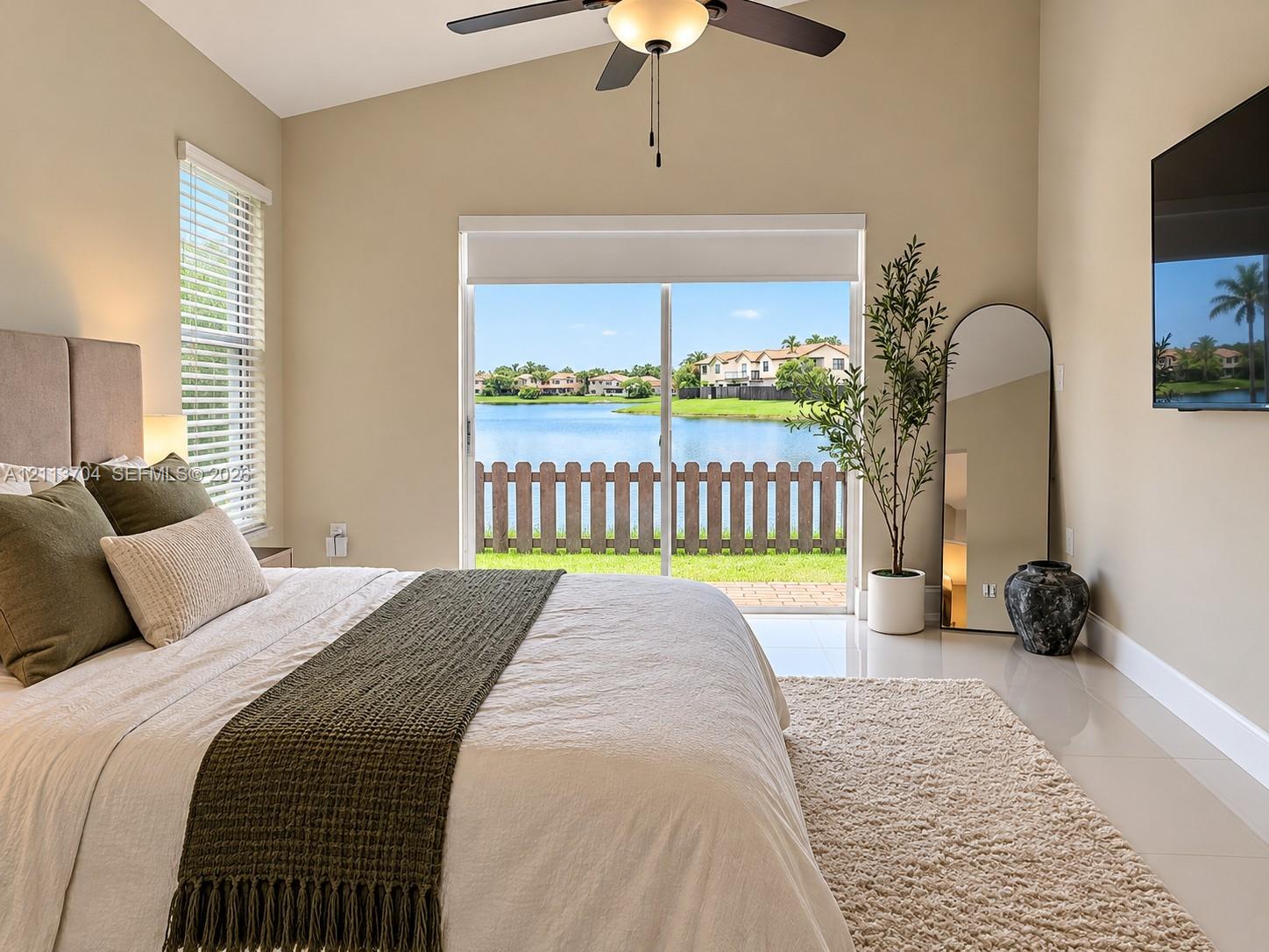 Vaulted ceiling with integrated lighted ceiling fan, tile flooring, and sliding glass doors opening to a waterfront backdrop