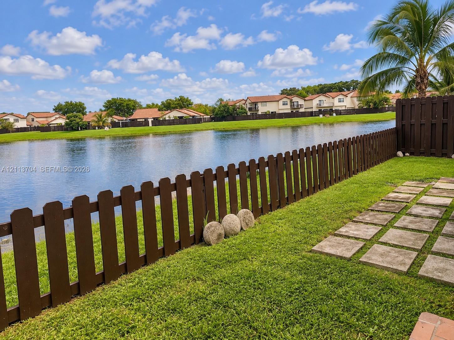 Waterfront backyard featuring a grass lawn, paved stone path, and dark wood-tone perimeter fencing