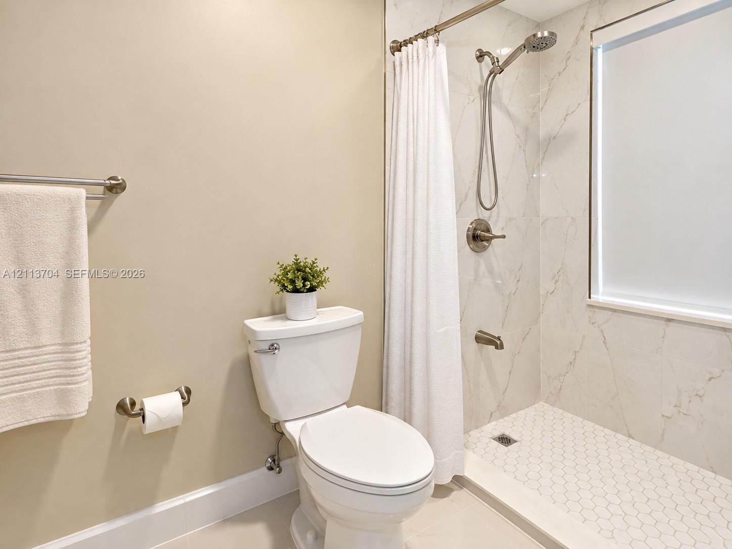 Full bathroom featuring large-format wall tile with natural veining, a hexagonal tile shower floor, brushed-finish fixtures, and a glass-enclosed window