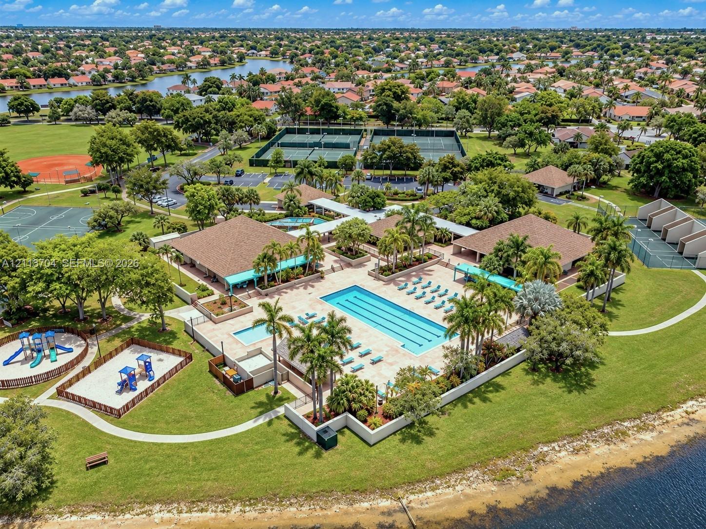 Community recreation complex featuring a lap-style swimming pool, multiple tennis courts, a basketball court, and a playground area, all situated within a waterfront setting