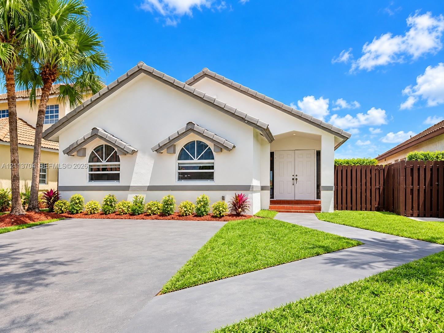 Single-story residence featuring a tile roof, stucco exterior, arched windows, dual-entry doors, and a concrete driveway Single-story residence featuring a tile roof, stucco exterior, arched windows, dual-entry doors, and a concrete driveway