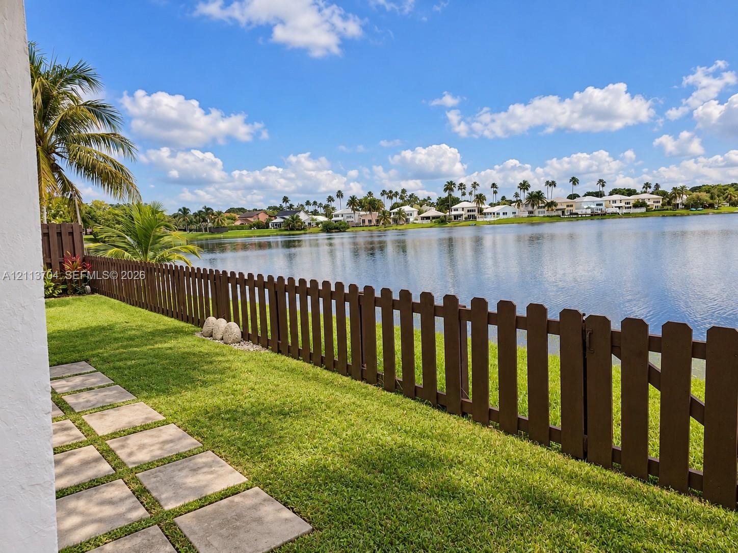 Waterfront lot featuring a grass lawn, paved stone path, and dark brown wood-finish picket fencing