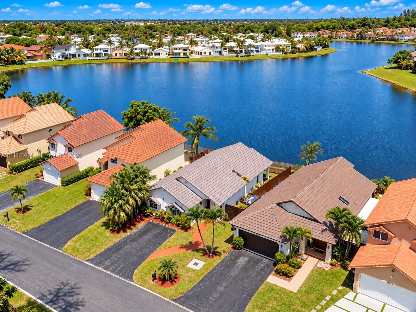 Waterfront residential property featuring tile roofing, asphalt driveways, mature palm trees, and manicured landscaping Waterfront residential property featuring tile roofing, asphalt driveways, mature palm trees, and manicured landscaping