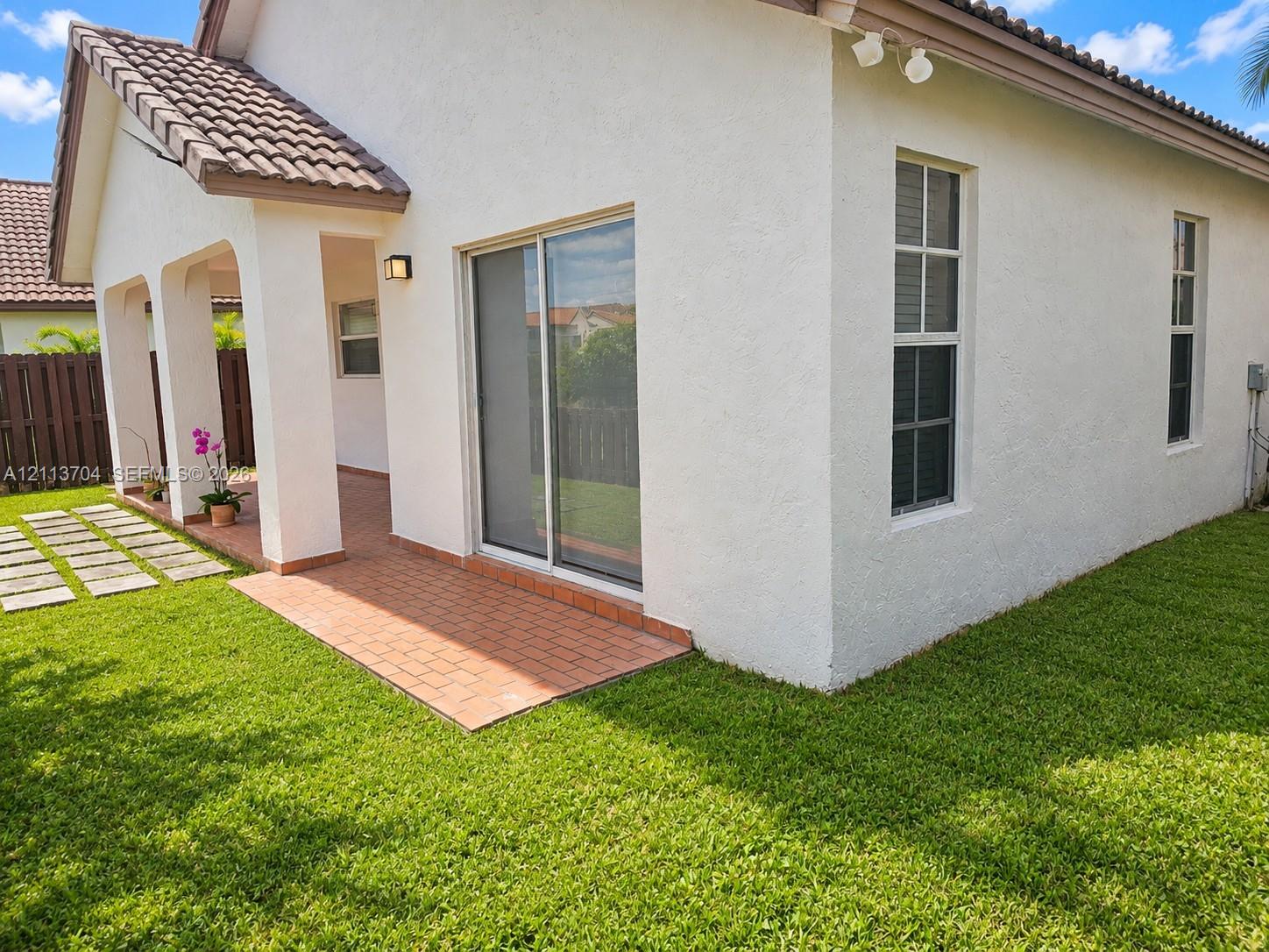 Stucco exterior featuring a covered patio, brick pavers, sliding glass doors, and a tiled roof