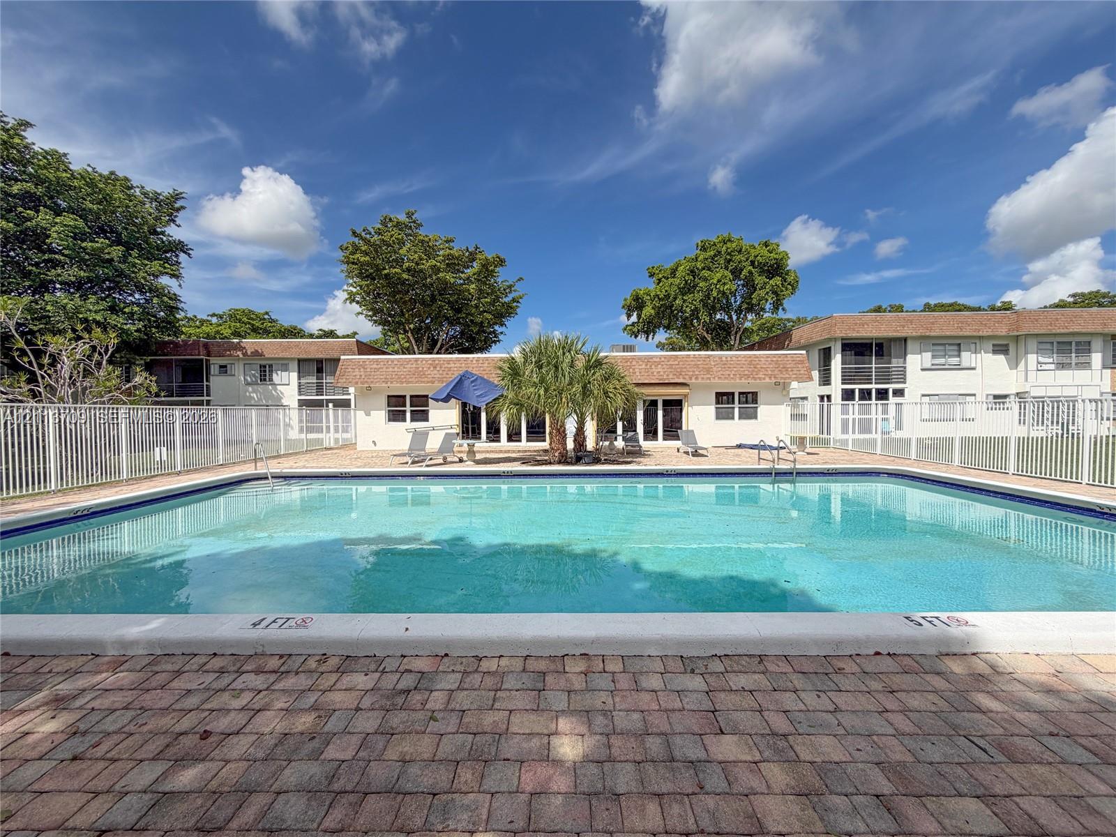 In-ground swimming pool featuring a brick paver deck and white metal fencing