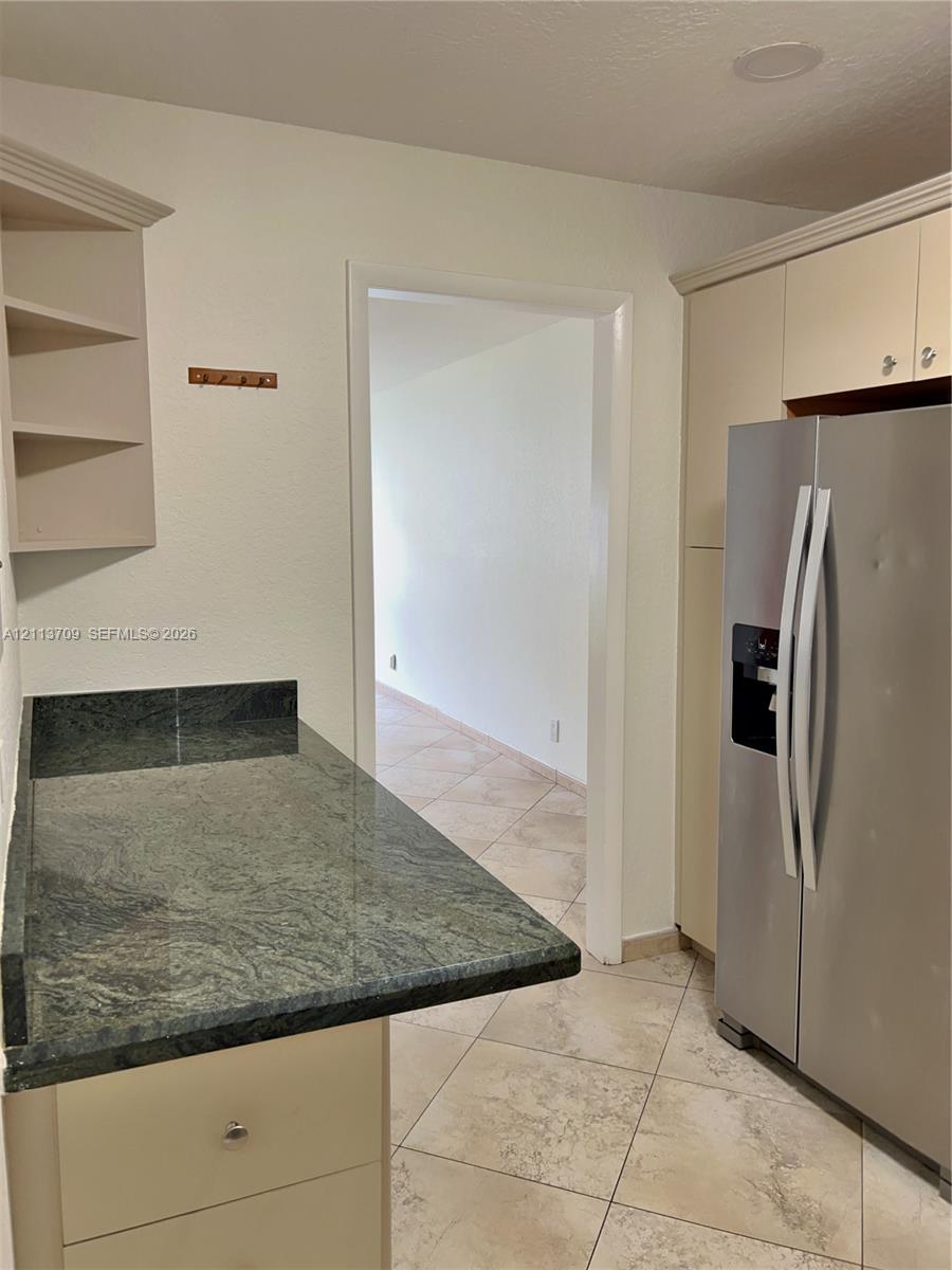 Kitchen featuring stone countertops, built-in cabinetry, an integrated refrigerator, open shelving, and tile flooring Kitchen featuring stone countertops, built-in cabinetry, an integrated refrigerator, open shelving, and tile flooring
