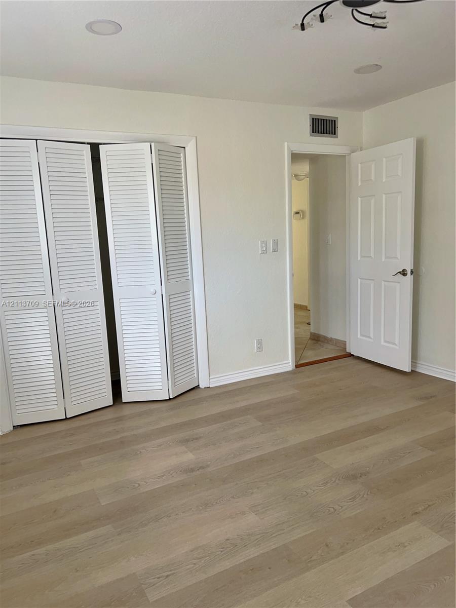Wood-finish flooring, white louvered bifold closet doors, recessed ceiling lighting, and a six-panel interior door Wood-finish flooring, white louvered bifold closet doors, recessed ceiling lighting, and a six-panel interior door