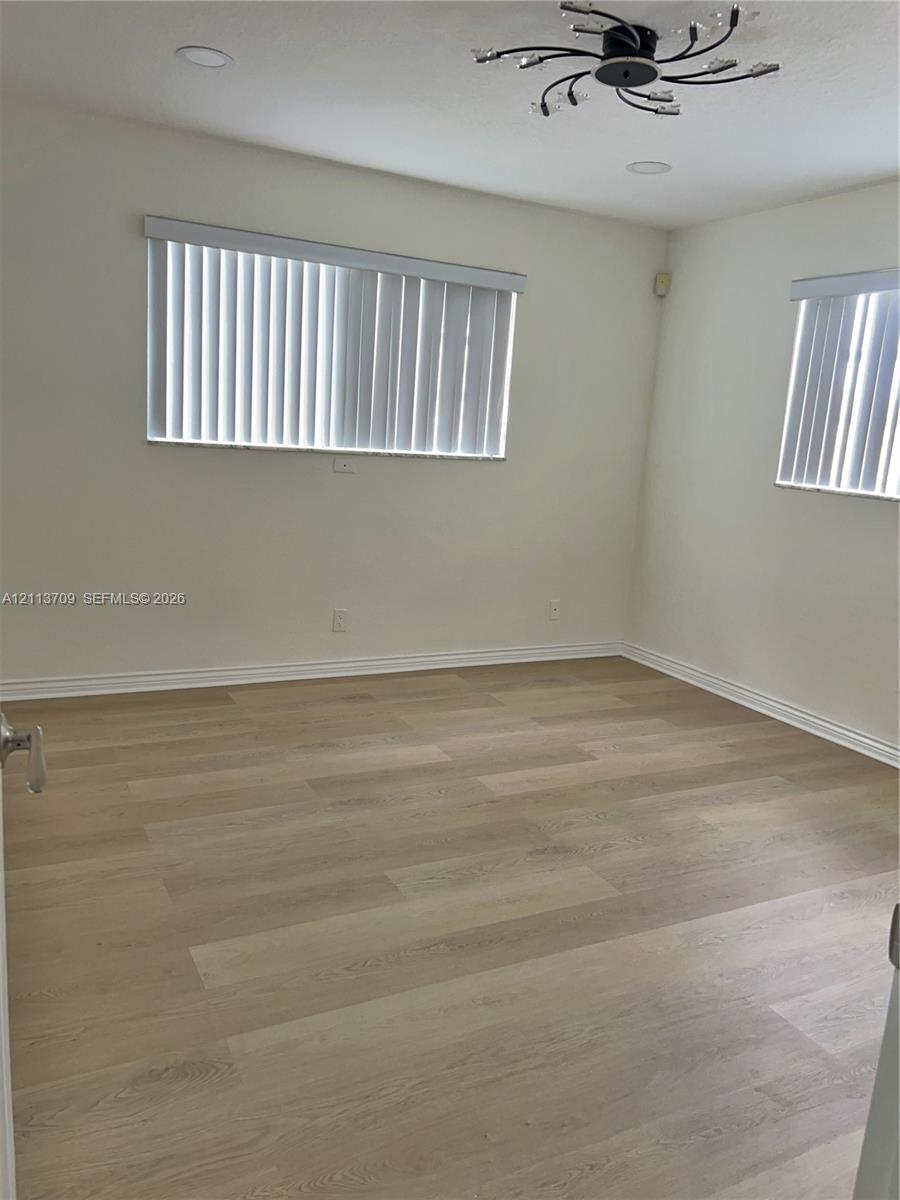 Light-filled room featuring wood-finish flooring, recessed lighting, a modern multi-arm ceiling fixture, and dual windows with vertical blinds Light-filled room featuring wood-finish flooring, recessed lighting, a modern multi-arm ceiling fixture, and dual windows with vertical blinds