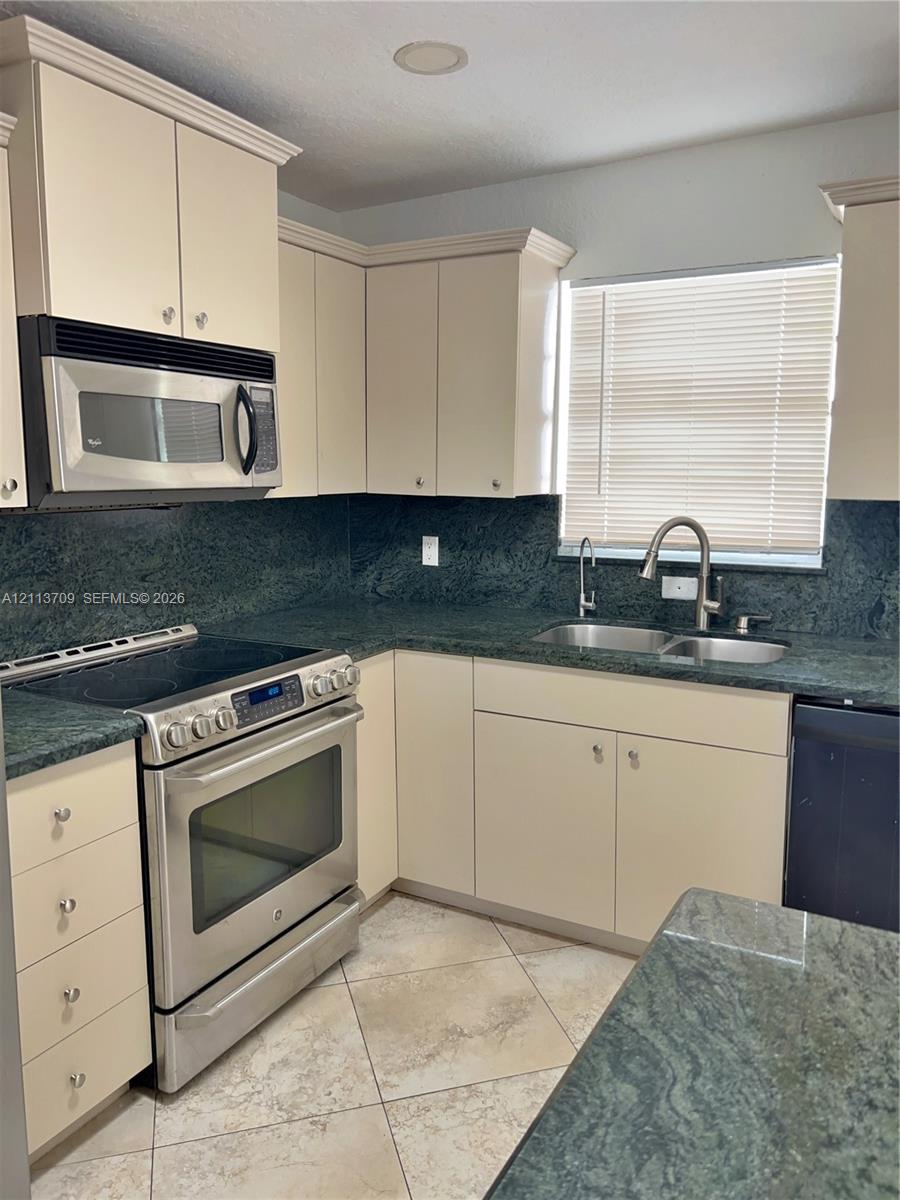 Kitchen featuring solid-surface countertops, custom shaker-style cabinetry, stainless steel appliances, a double-basin undermount sink with a gooseneck faucet, and tiled flooring Kitchen featuring solid-surface countertops, custom shaker-style cabinetry, stainless steel appliances, a double-basin undermount sink with a gooseneck faucet, and tiled flooring