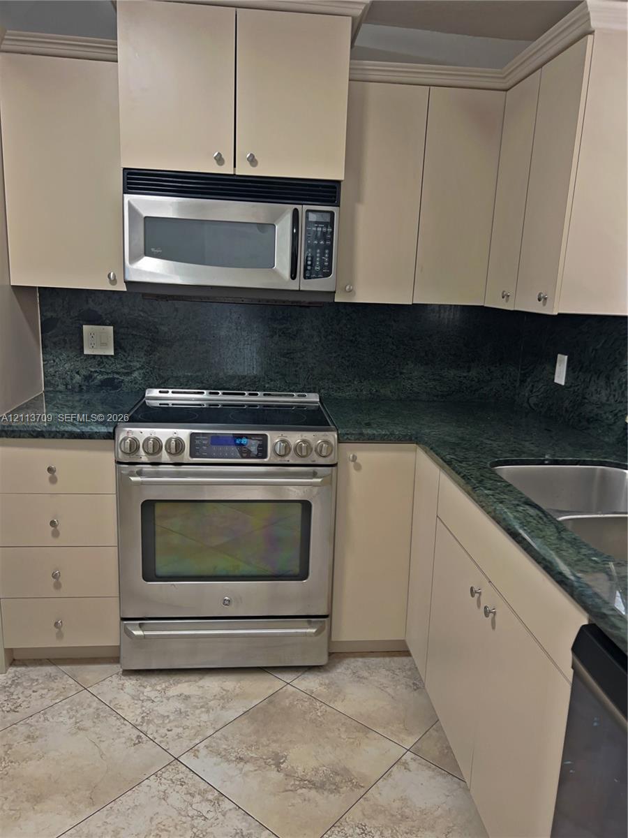 Kitchen featuring stone countertops, stainless steel appliances, upper and lower cabinetry, a dual-basin undermount sink, and tile flooring Kitchen featuring stone countertops, stainless steel appliances, upper and lower cabinetry, a dual-basin undermount sink, and tile flooring