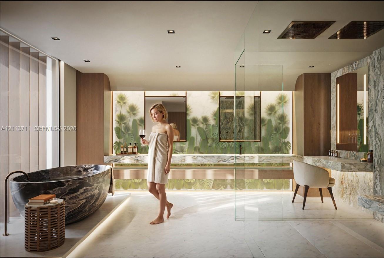Freestanding oval stone soaking tub with floor-mounted faucet, dual-sink stone vanity, recessed lighting, glass-enclosed shower, and built-in vanity station