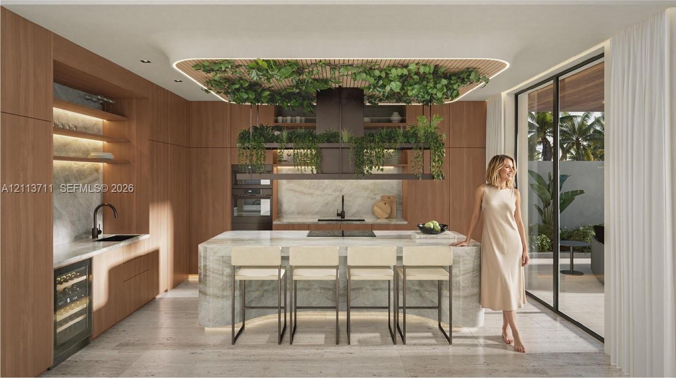 Modern kitchen featuring full-height wood-finish cabinetry, a waterfall-edge stone island, built-in wine refrigeration, integrated ceiling lighting, and floor-to-ceiling glass sliding doors