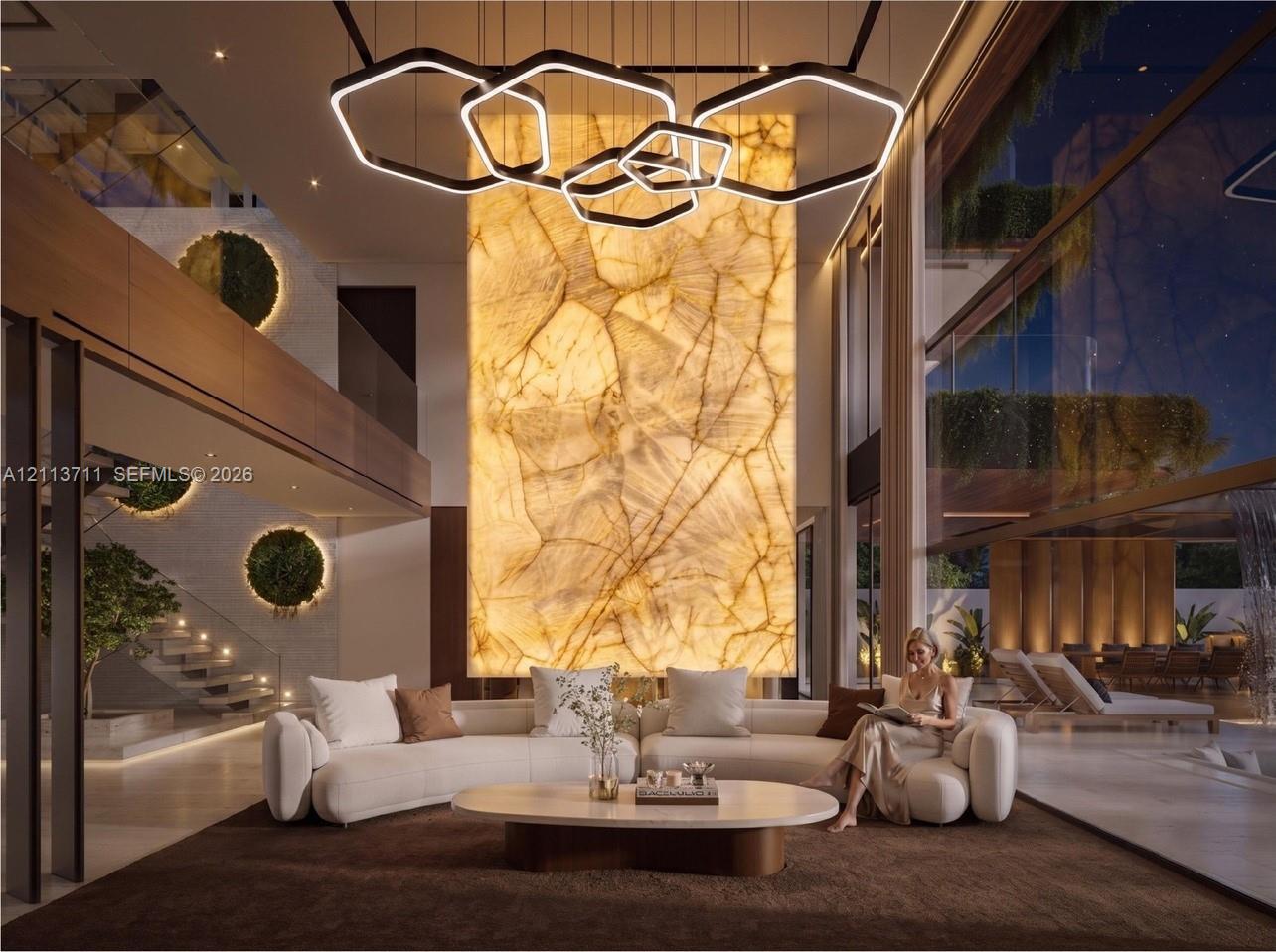 Double-height living area featuring a floor-to-ceiling backlit stone accent wall, multi-tiered geometric pendant lighting, full-height glass walls, and a glass-paneled staircase
