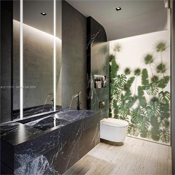 Custom stone vanity featuring a built-in basin and integrated lighting, wall-mounted toilet, recessed shelving, and large-format paneling