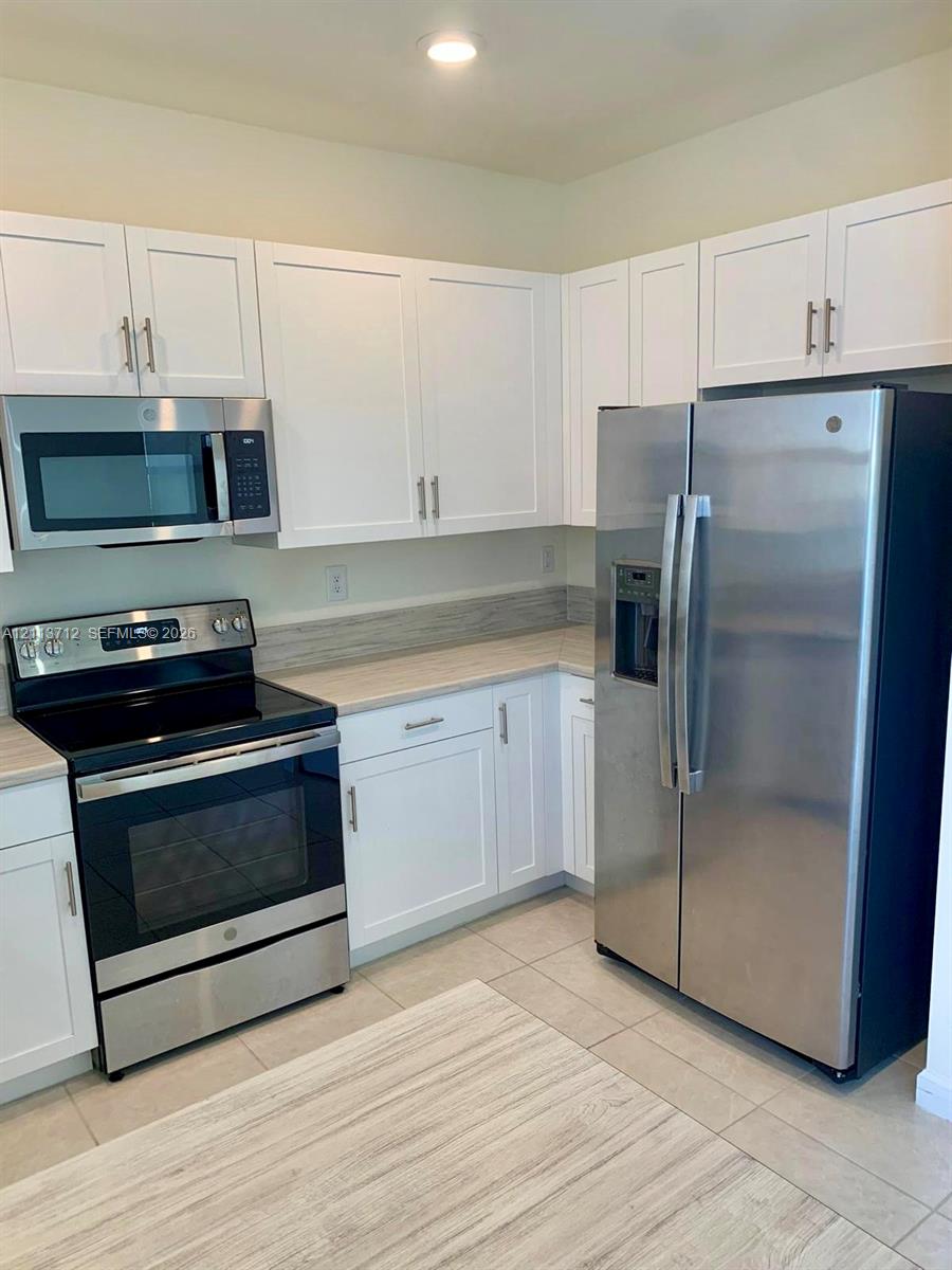 Kitchen featuring white shaker-style cabinetry, stainless steel appliances, neutral countertops, and tile flooring