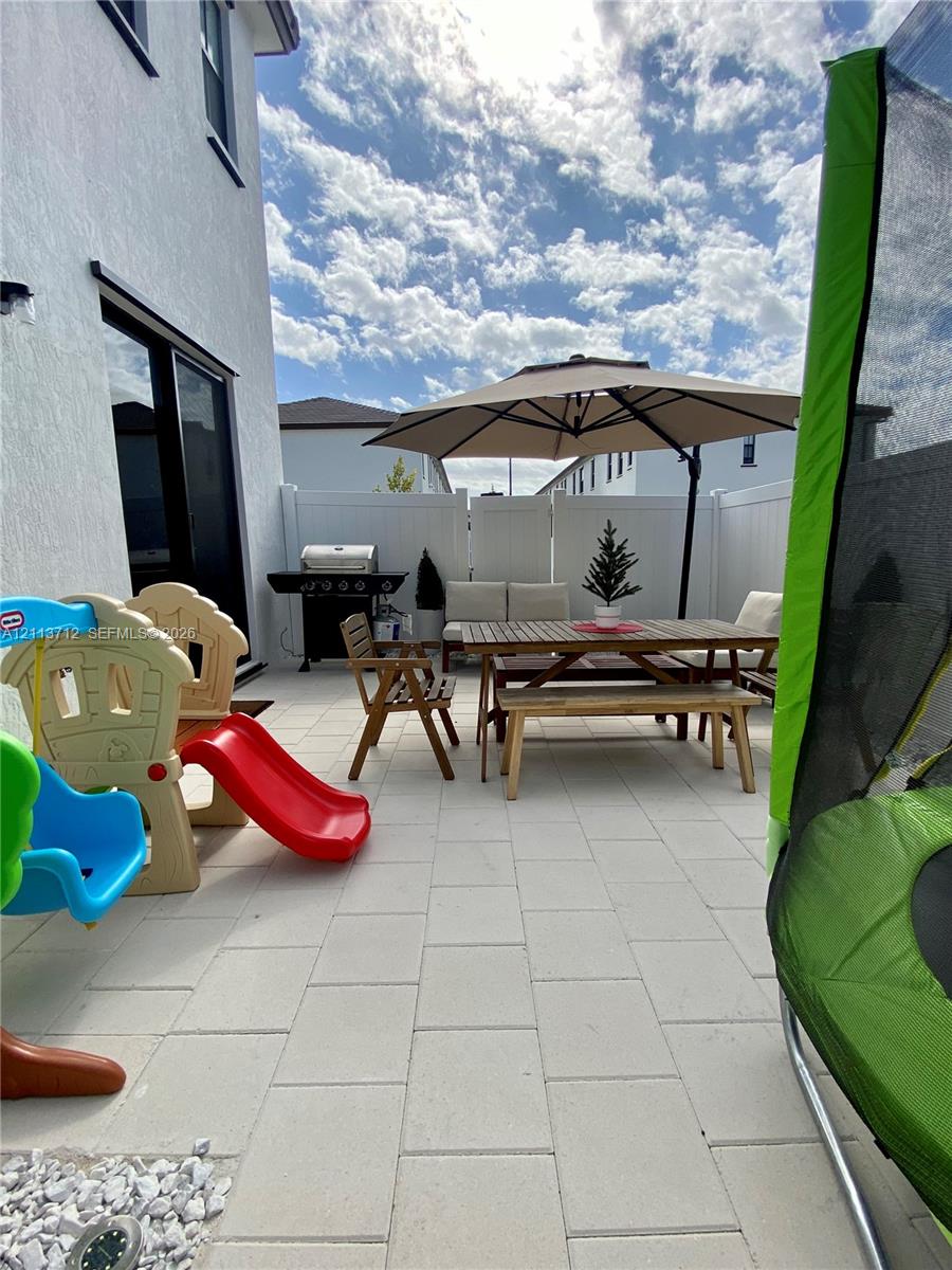 Patio area featuring light-toned concrete pavers, full-height white vinyl perimeter fencing, and a smooth stucco exterior finish