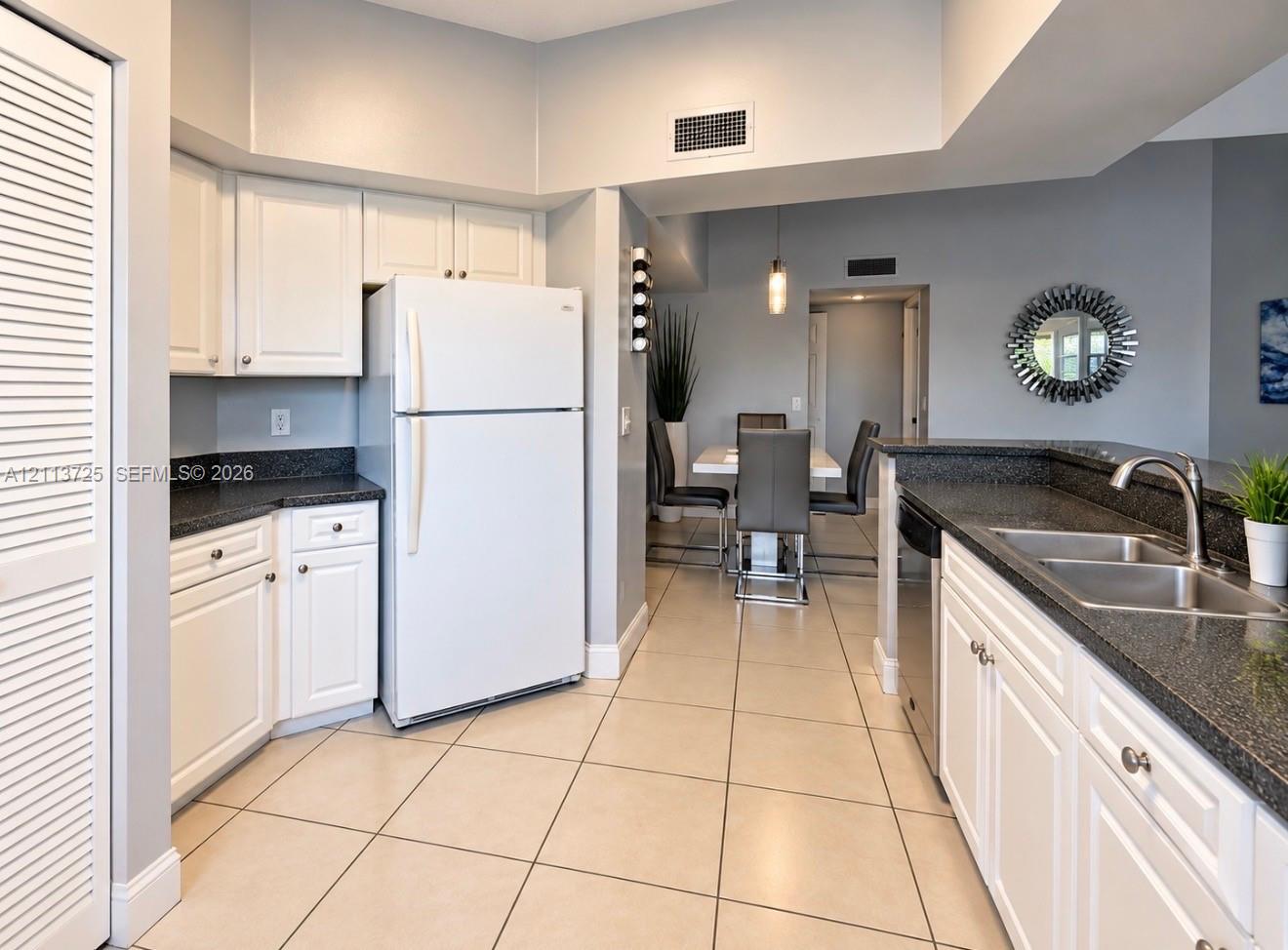 Kitchen featuring white shaker-style cabinetry, dark stone-finish countertops, stainless steel dual-basin sink with arched faucet, and tile flooring