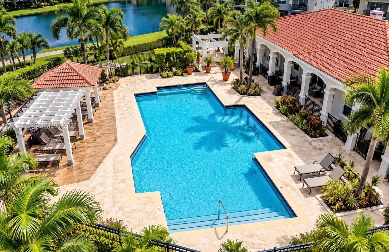 Swimming pool with a stone paver deck, white pergola, tile roof, and waterfront surroundings