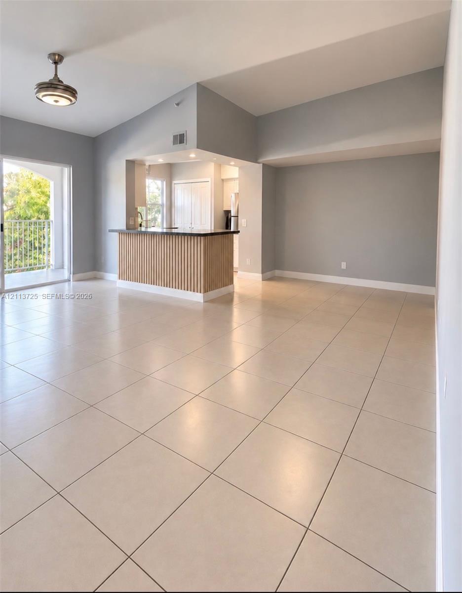 Open living area featuring vaulted ceilings, neutral floor tiling, a slatted wood-finish breakfast bar, and access to a private balcony Open living area featuring vaulted ceilings, neutral floor tiling, a slatted wood-finish breakfast bar, and access to a private balcony