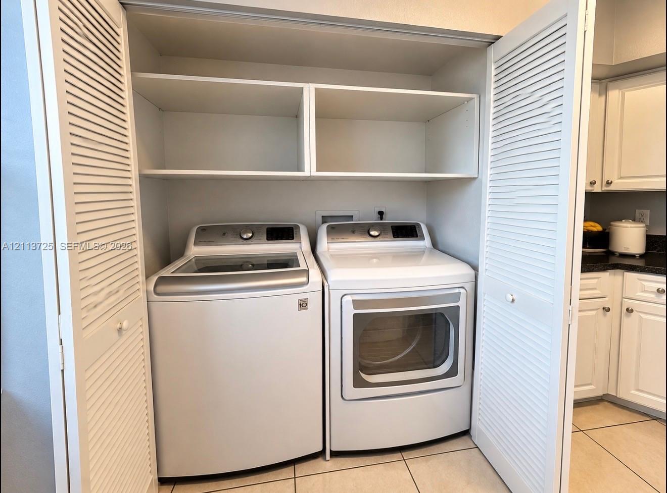 Laundry closet featuring louvered bi-fold doors, white upper shelving, and tiled flooring Laundry closet featuring louvered bi-fold doors, white upper shelving, and tiled flooring