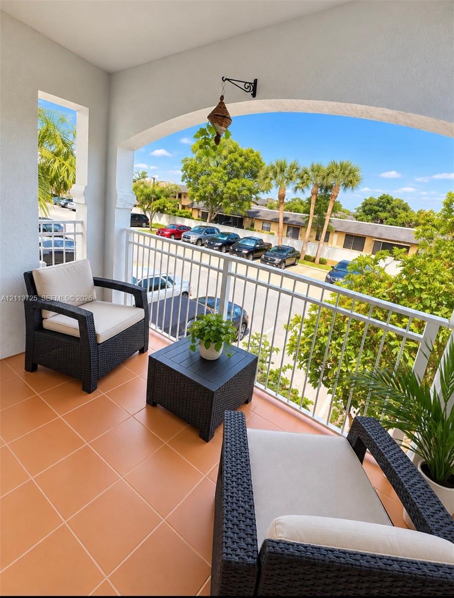 Covered balcony featuring a white metal railing, arched ceiling detail, and ceramic tile flooring Covered balcony featuring a white metal railing, arched ceiling detail, and ceramic tile flooring