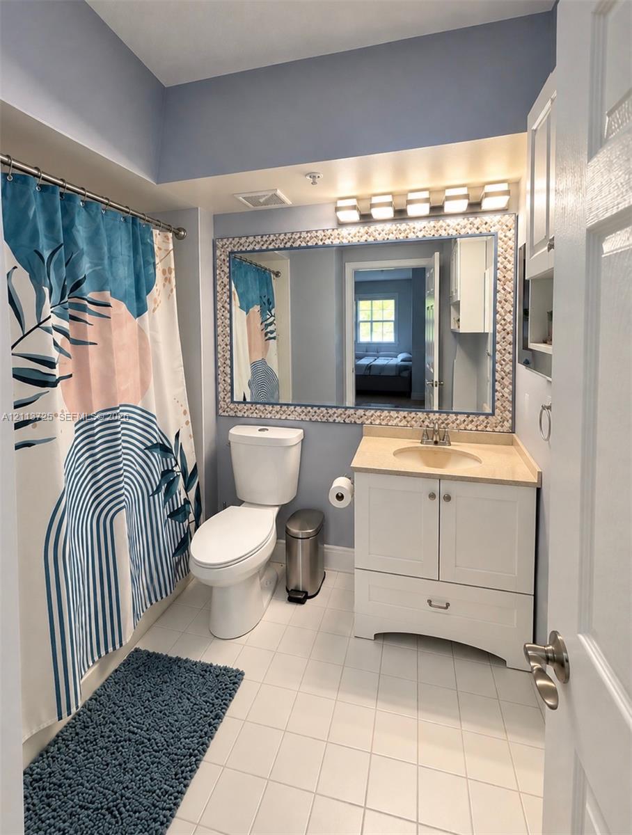 Bathroom featuring a white vanity cabinet with a stone-top integrated sink, a large framed wall mirror, a five-light vanity fixture, and tiled flooring Bathroom featuring a white vanity cabinet with a stone-top integrated sink, a large framed wall mirror, a five-light vanity fixture, and tiled flooring