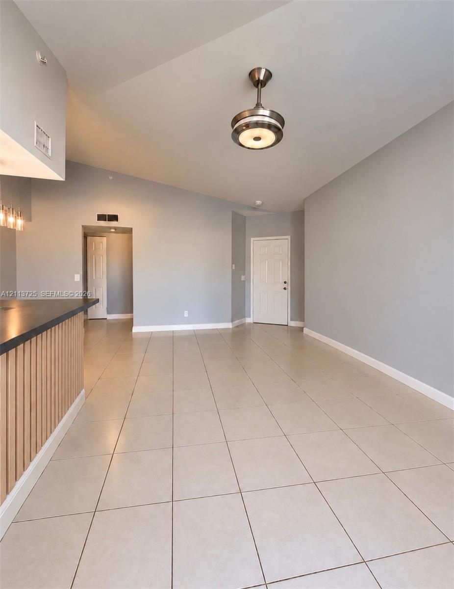 Vaulted ceilings, large-format tile flooring, a breakfast bar featuring vertical wood-slat detailing, and a contemporary semi-flush mount light fixture Vaulted ceilings, large-format tile flooring, a breakfast bar featuring vertical wood-slat detailing, and a contemporary semi-flush mount light fixture