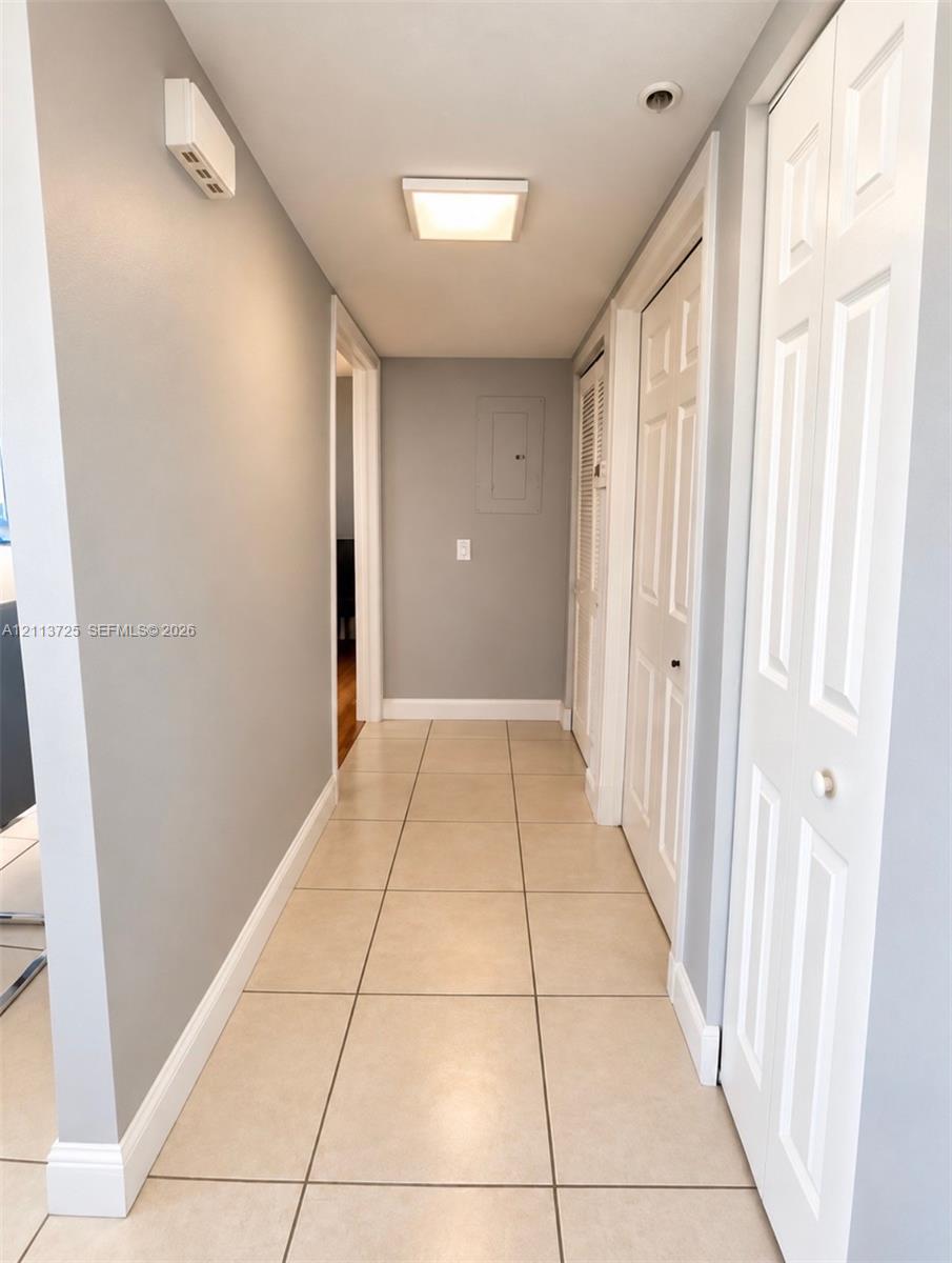 Hallway featuring neutral-toned tile flooring, recessed ceiling lighting, and multiple interior paneled doors