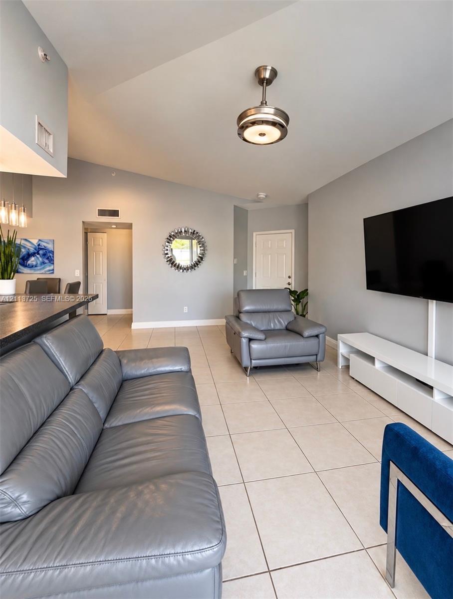 Living area featuring a vaulted ceiling, neutral tile flooring, and a modern drum-style flush-mount light fixture Living area featuring a vaulted ceiling, neutral tile flooring, and a modern drum-style flush-mount light fixture