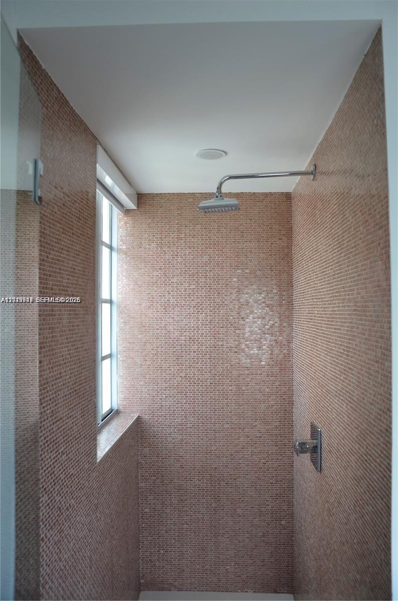 Shower stall featuring floor-to-ceiling mosaic tile, wall-mounted rainfall showerhead, single-handle pressure balance valve, and a window with a glass pane